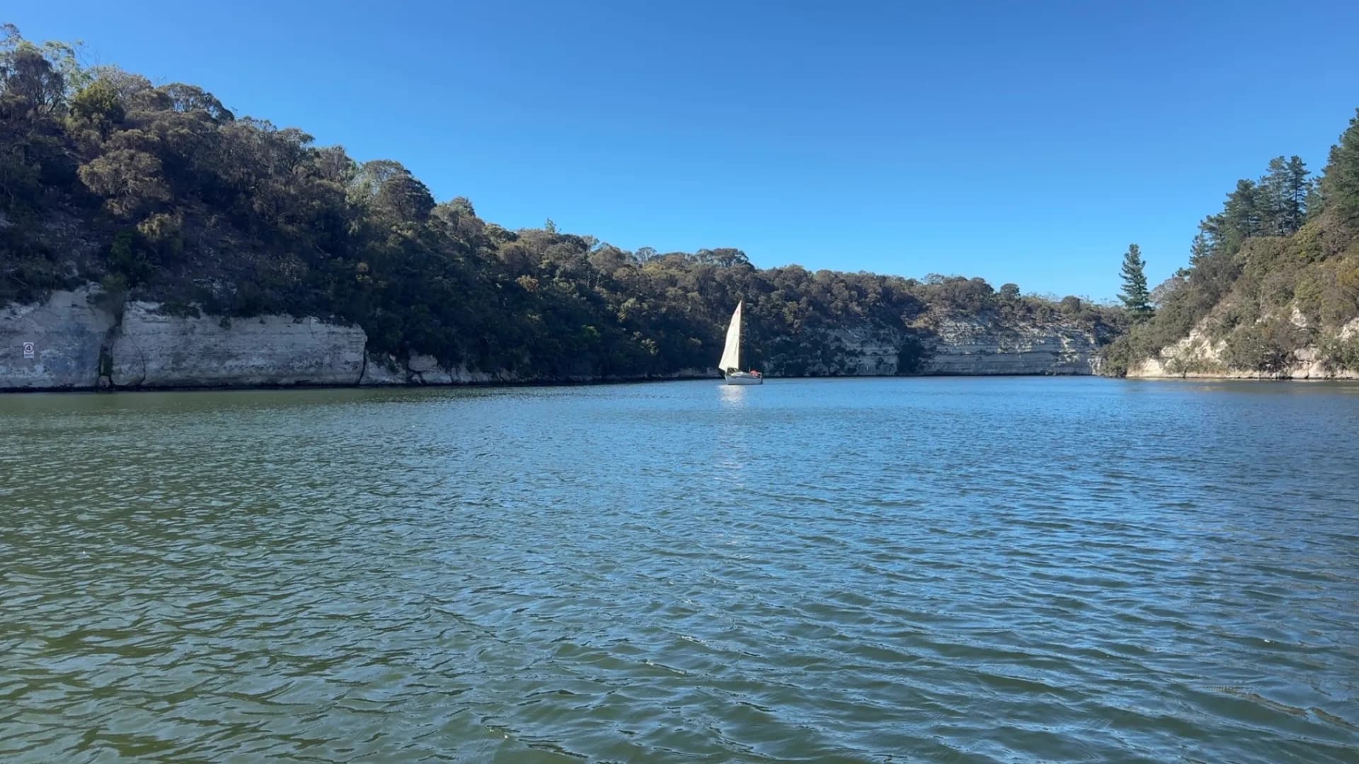 A yacht under sail on the Glenelg River beneath the limestone cliffs