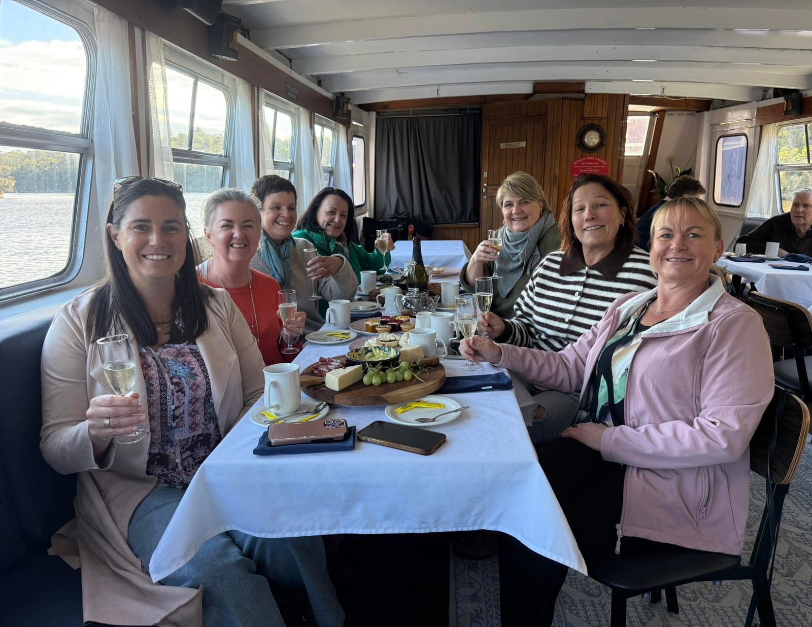 Guests raising a glass over a grazing board at the long table in MV Mini Munya's cabin on a lunch cruise